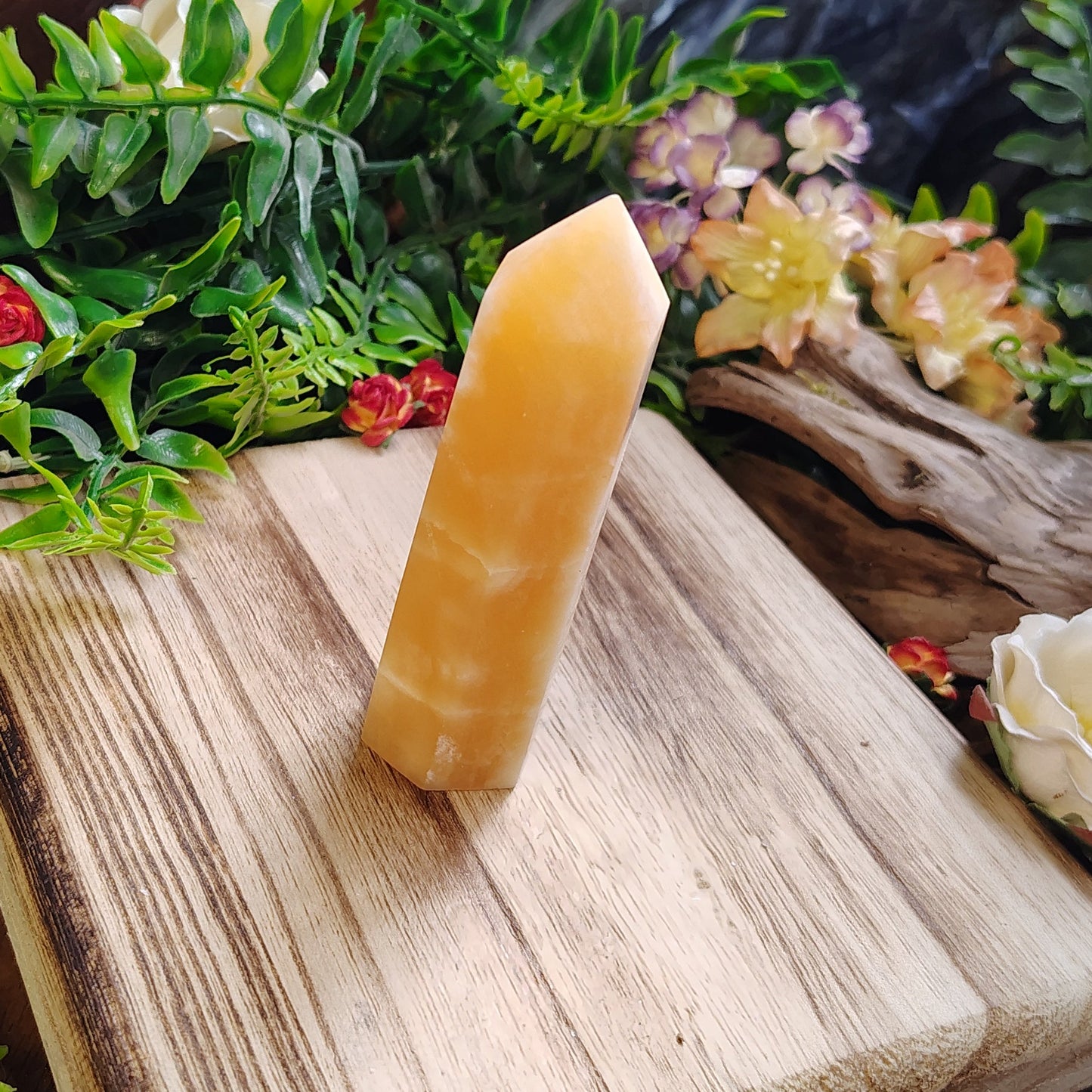 yellow crystal on a wooden block with greenery and flowers in the background