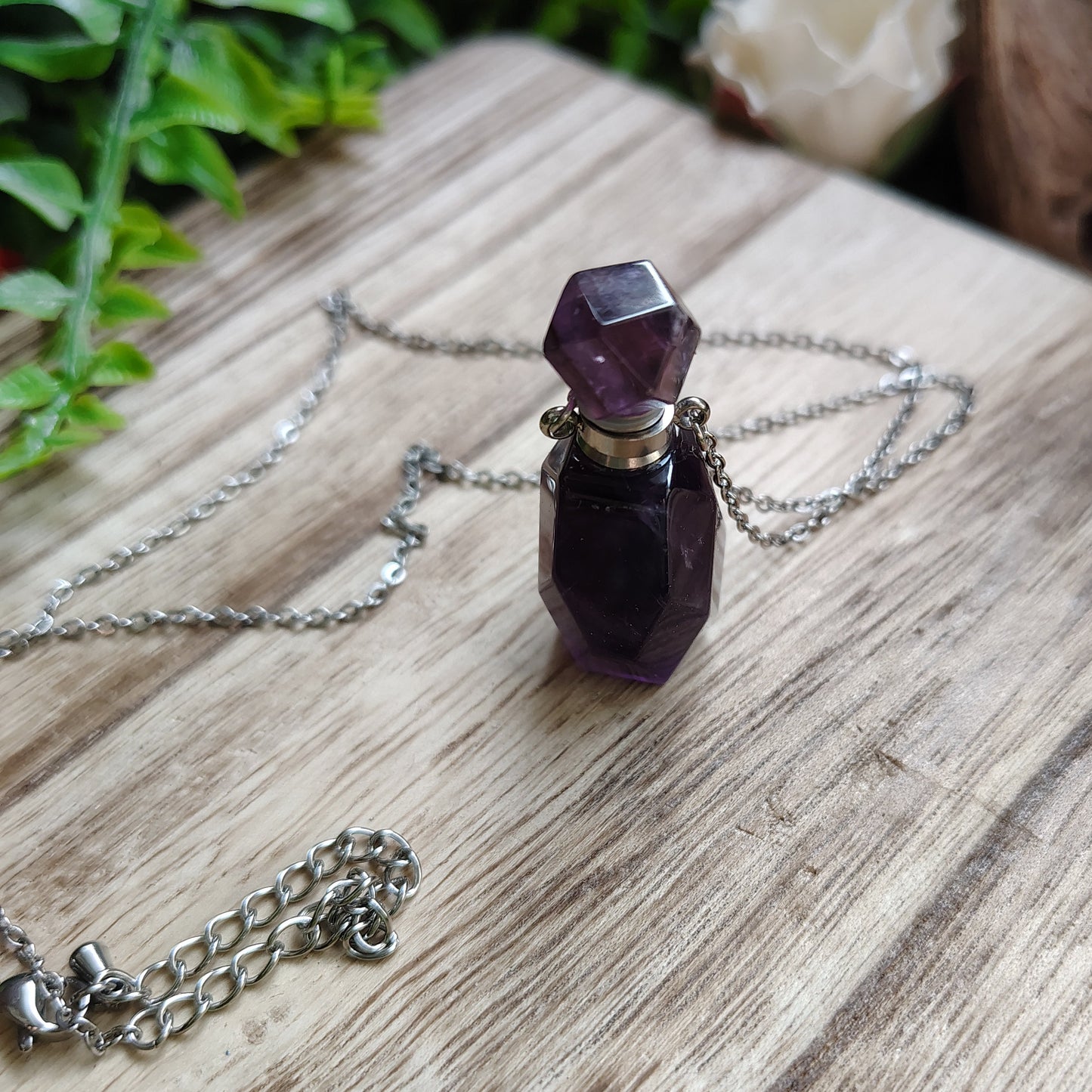 Amethyst crystal necklace on a wooden surface with greenery
