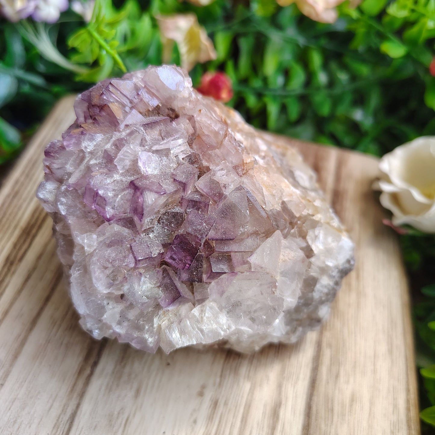 fluorite crystal cluster on a wooden surface with greenery in the background