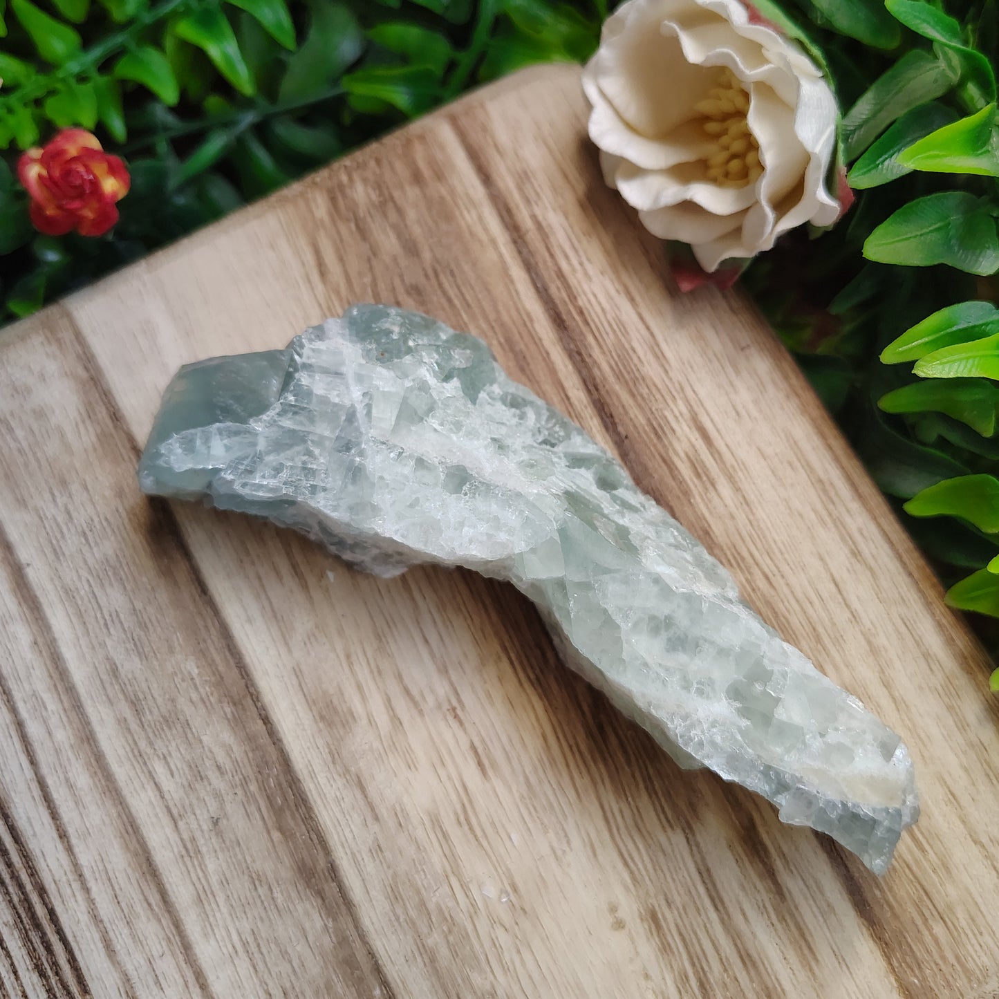 Crystal on a wooden surface with greenery and flowers in the background