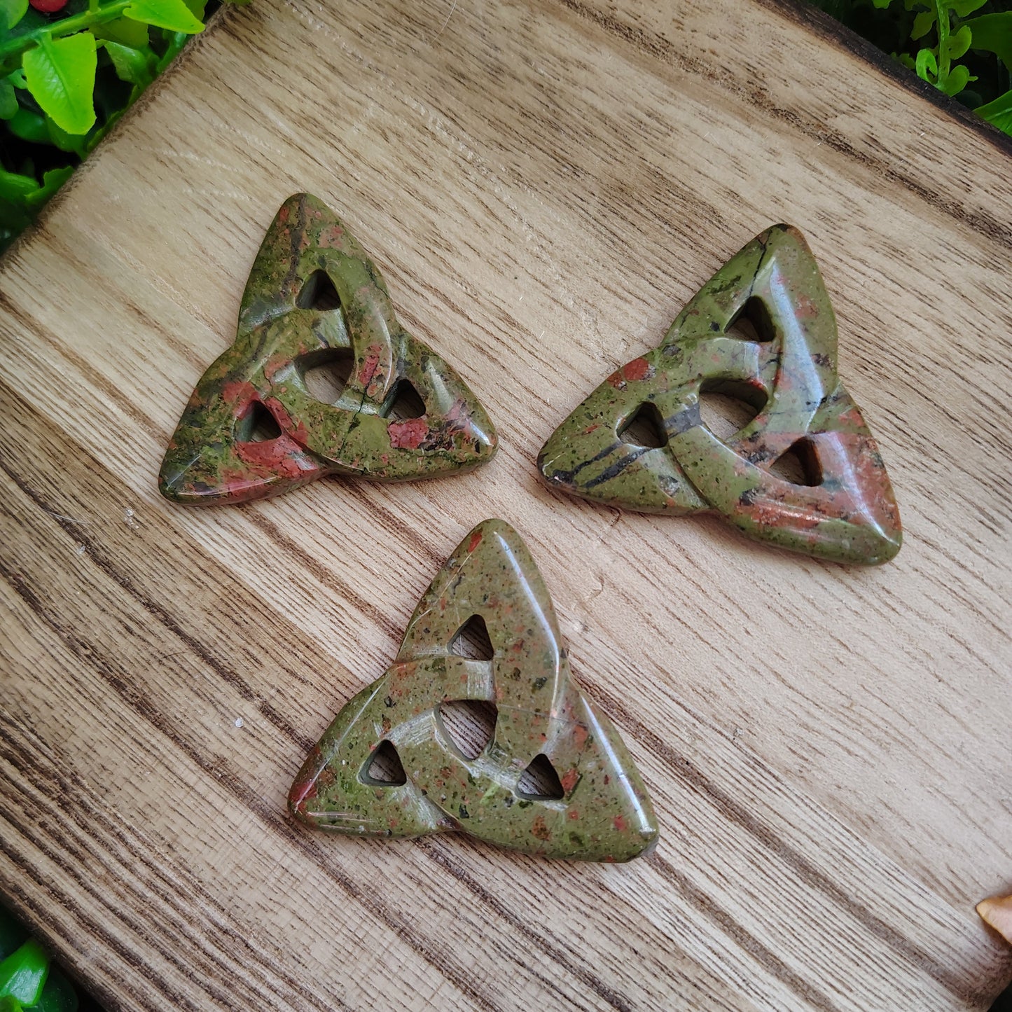 Three green stone triangular pieces with cut-out patterns on a wooden surface.