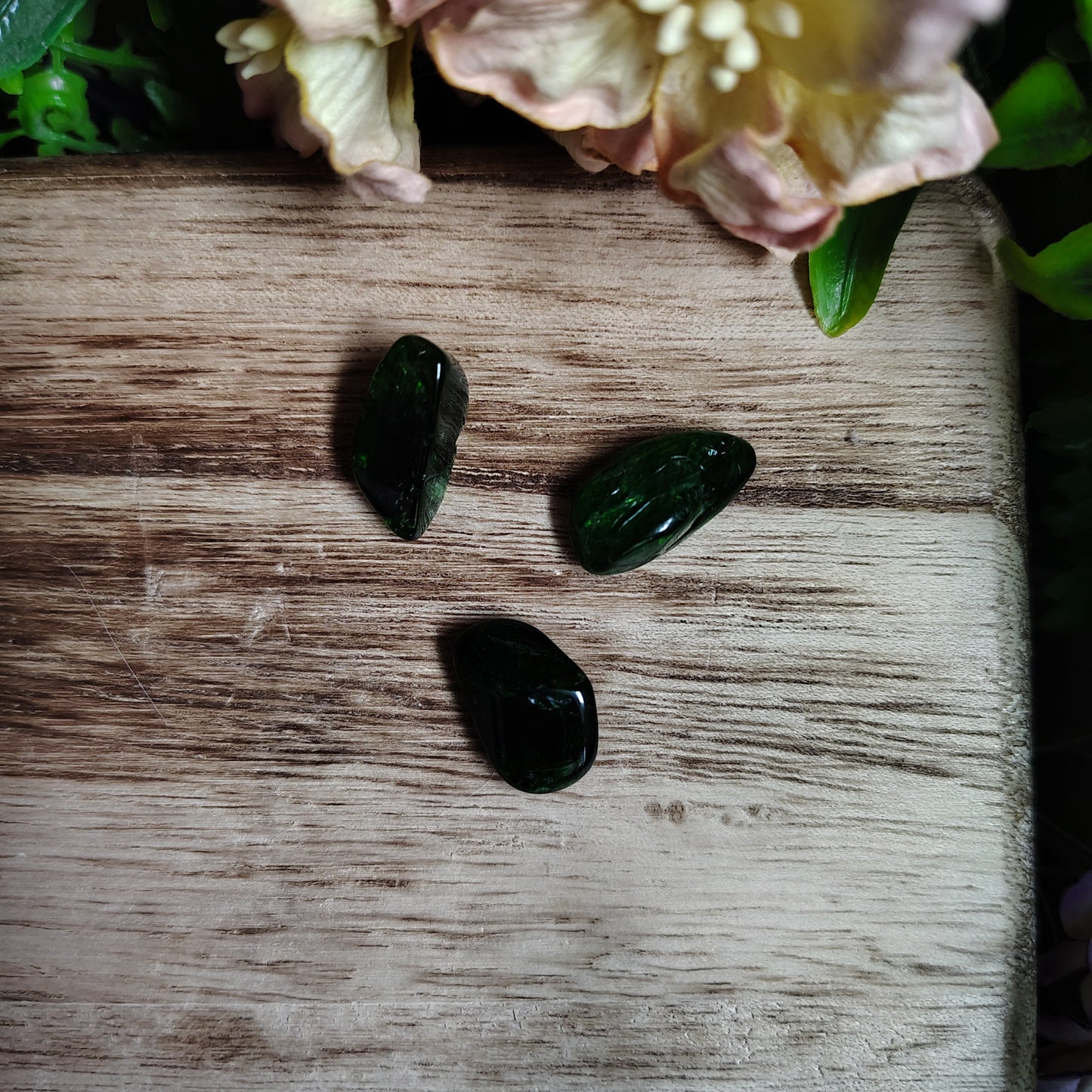 Three dark objects on a wooden surface with a pink flower to the left.