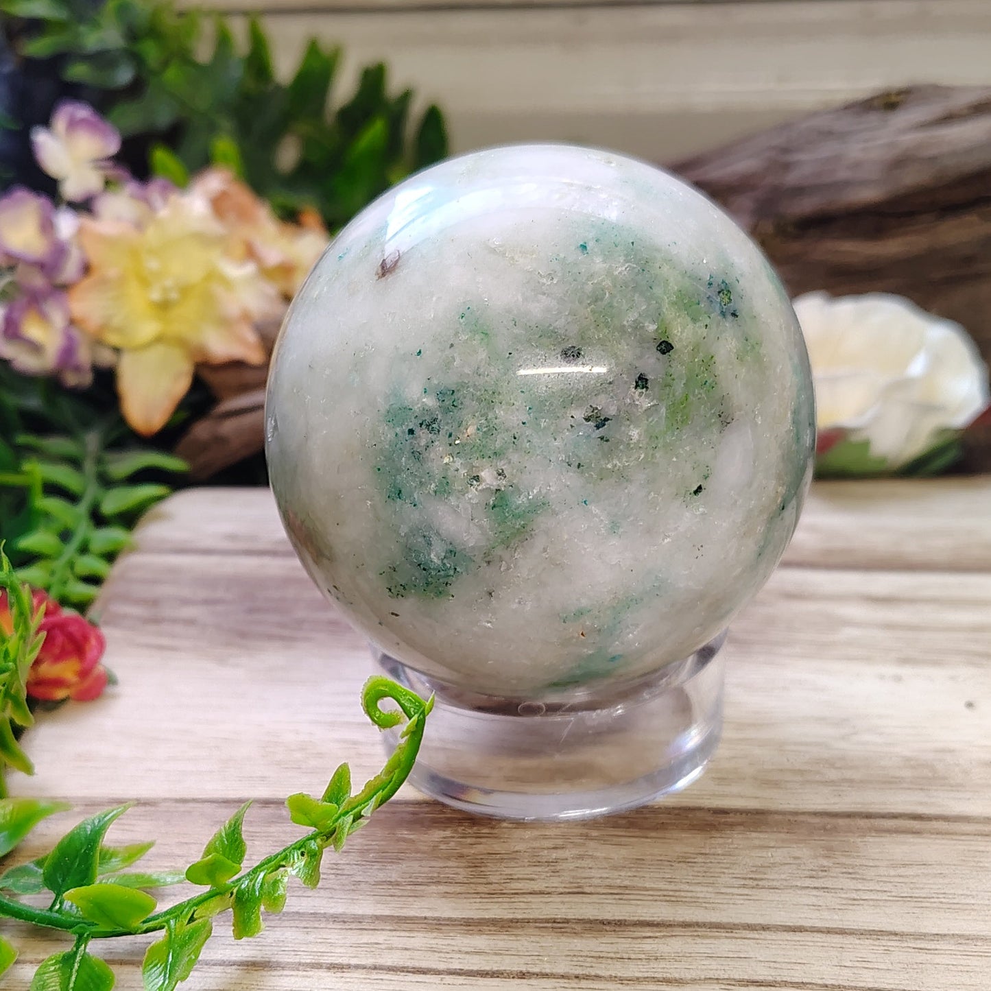 Crystal ball on a wooden stand with plants and flowers in the background