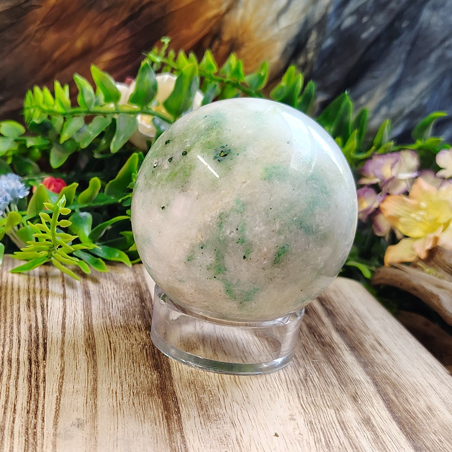 Crystal ball on a wooden stand with plants and flowers in the background