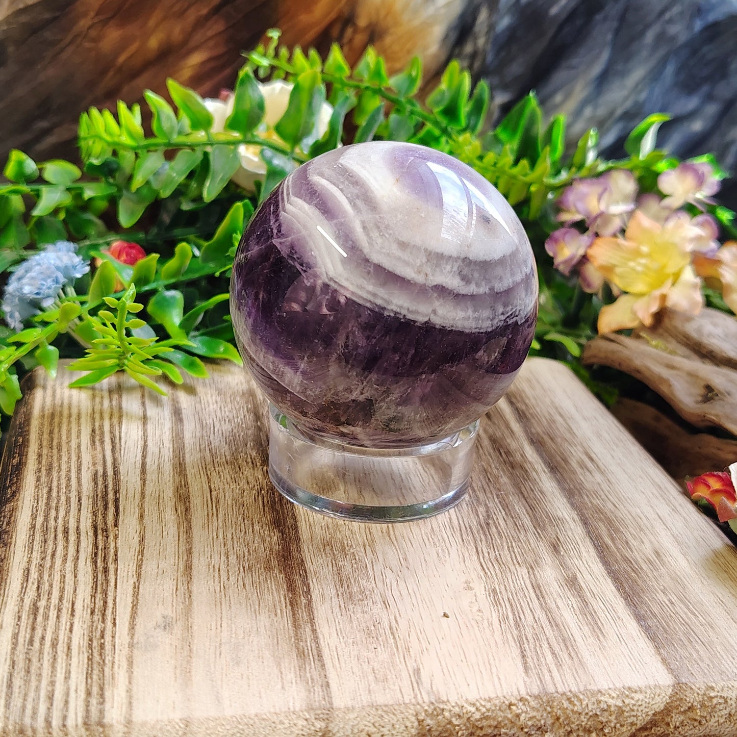 Amethyst crystal ball on a wooden stand with plants and flowers in the background