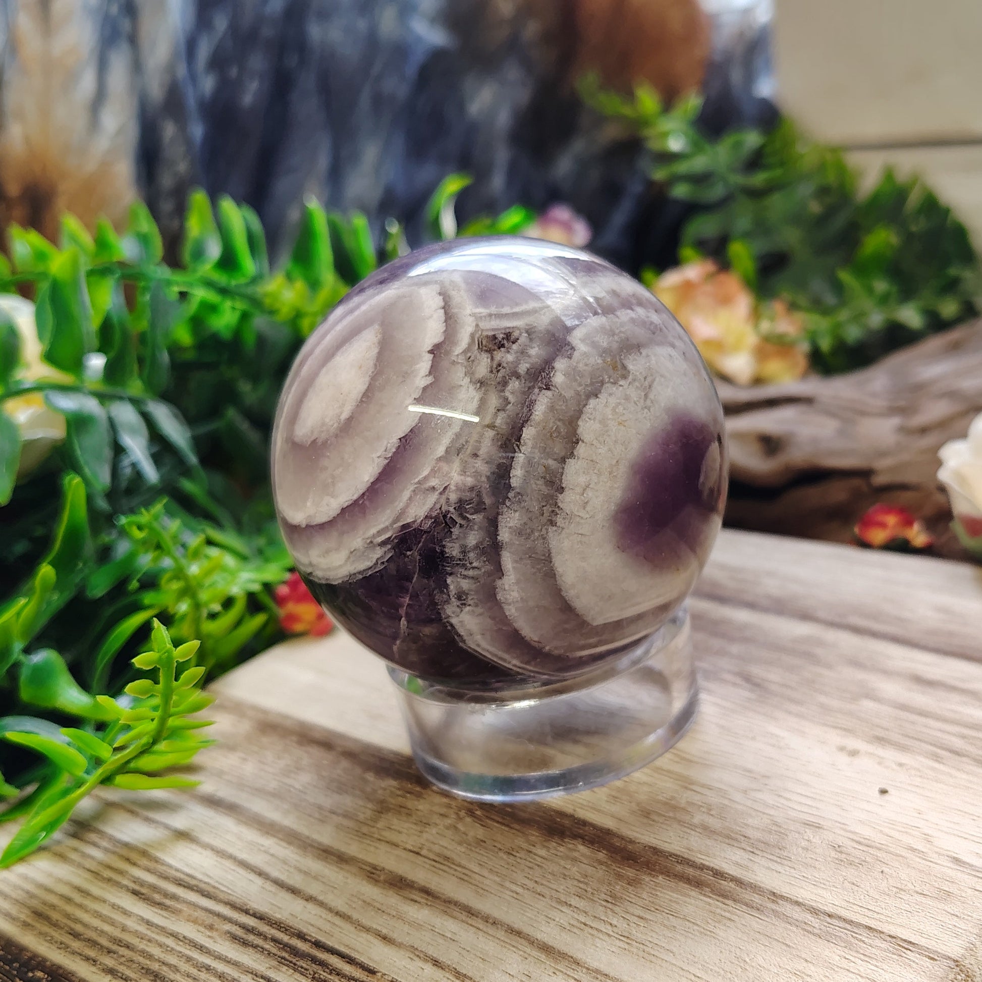 Decorative amethyst sphere on a wooden surface with greenery and flowers in the background