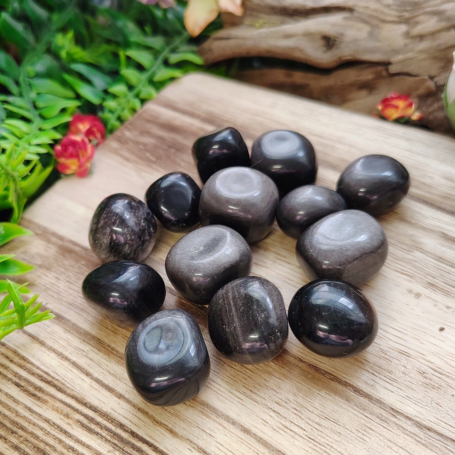 Black stones on a wooden surface with greenery and flowers in the background