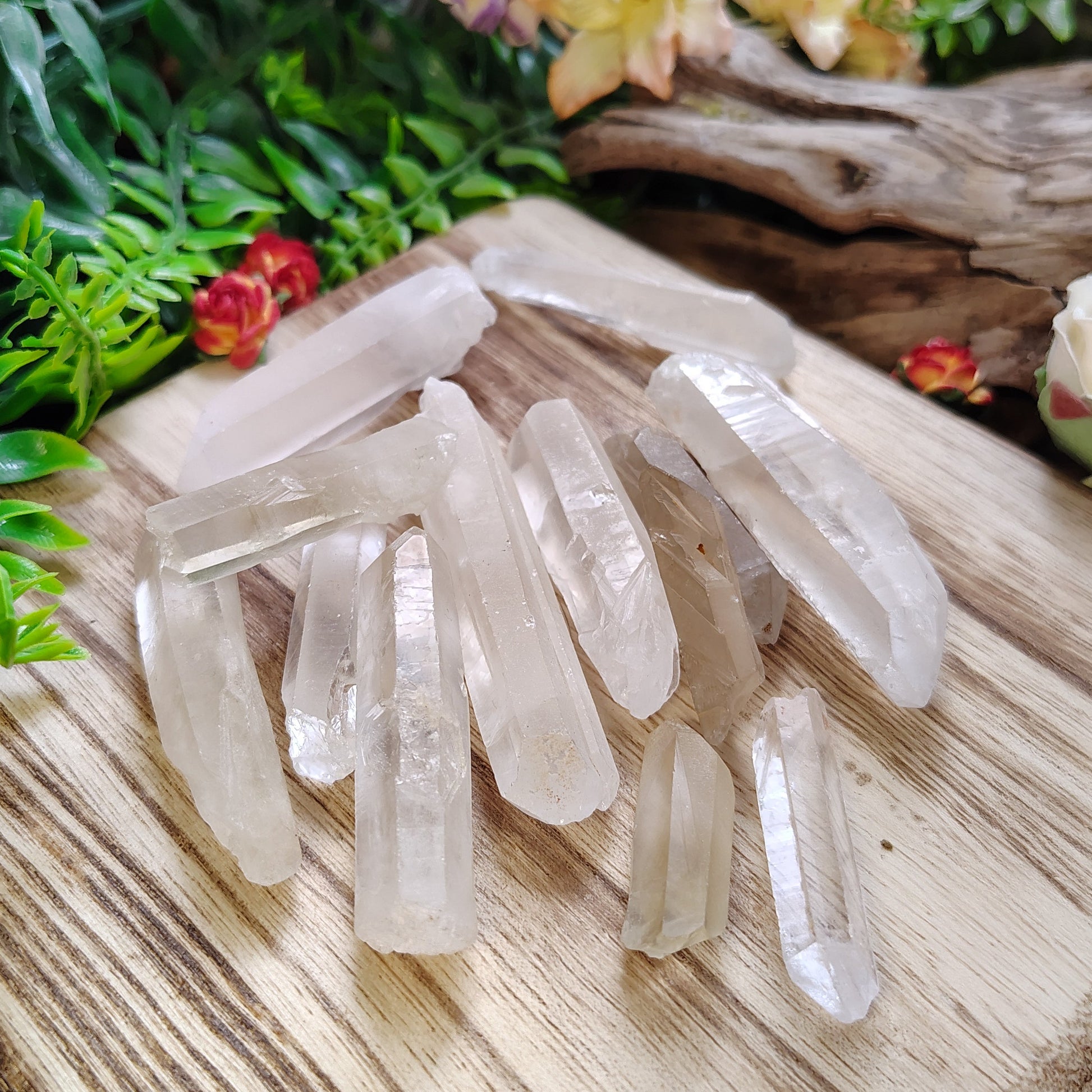 Clear crystal points on a wooden surface with greenery and flowers in the background
