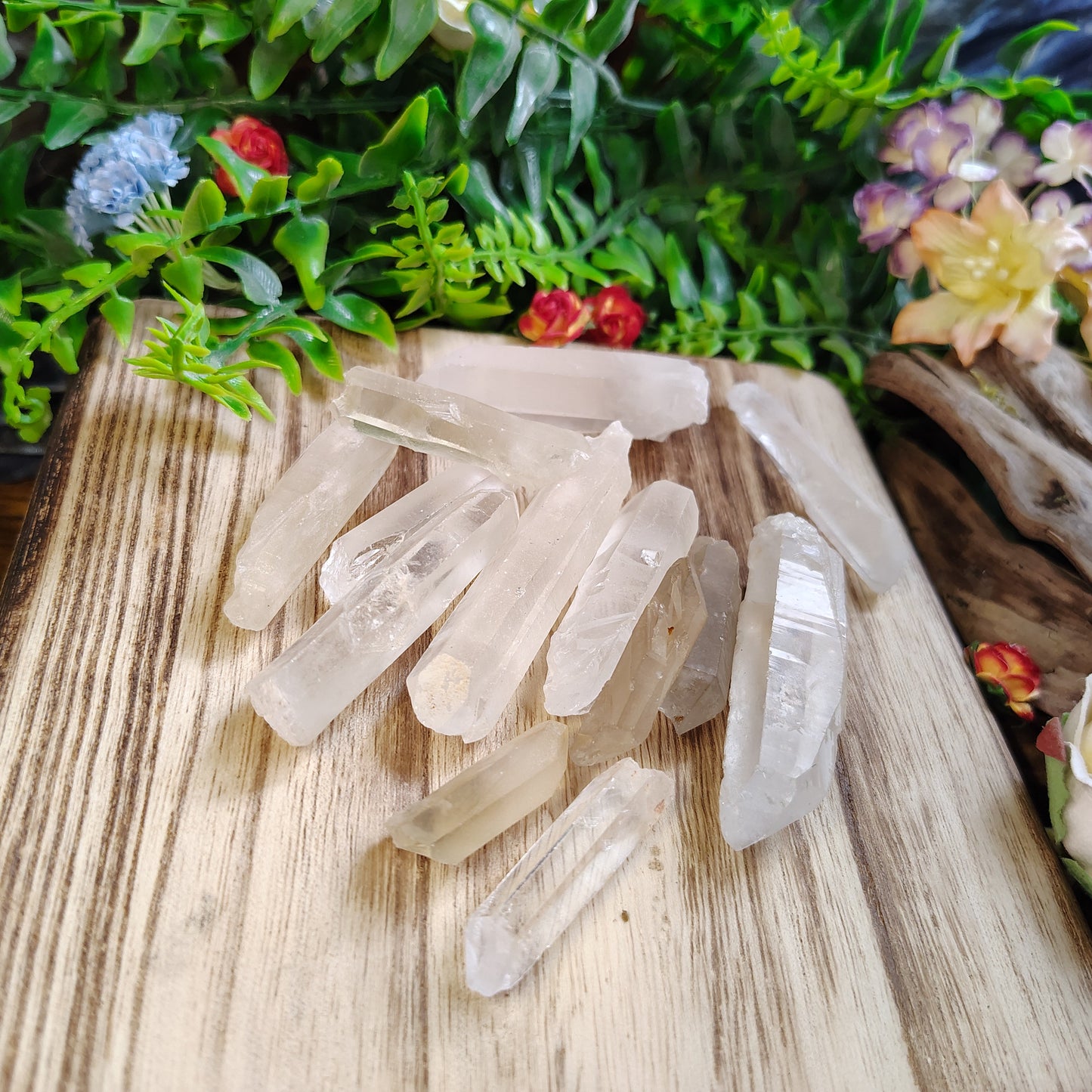Clear crystal points on a wooden surface with greenery and flowers in the background