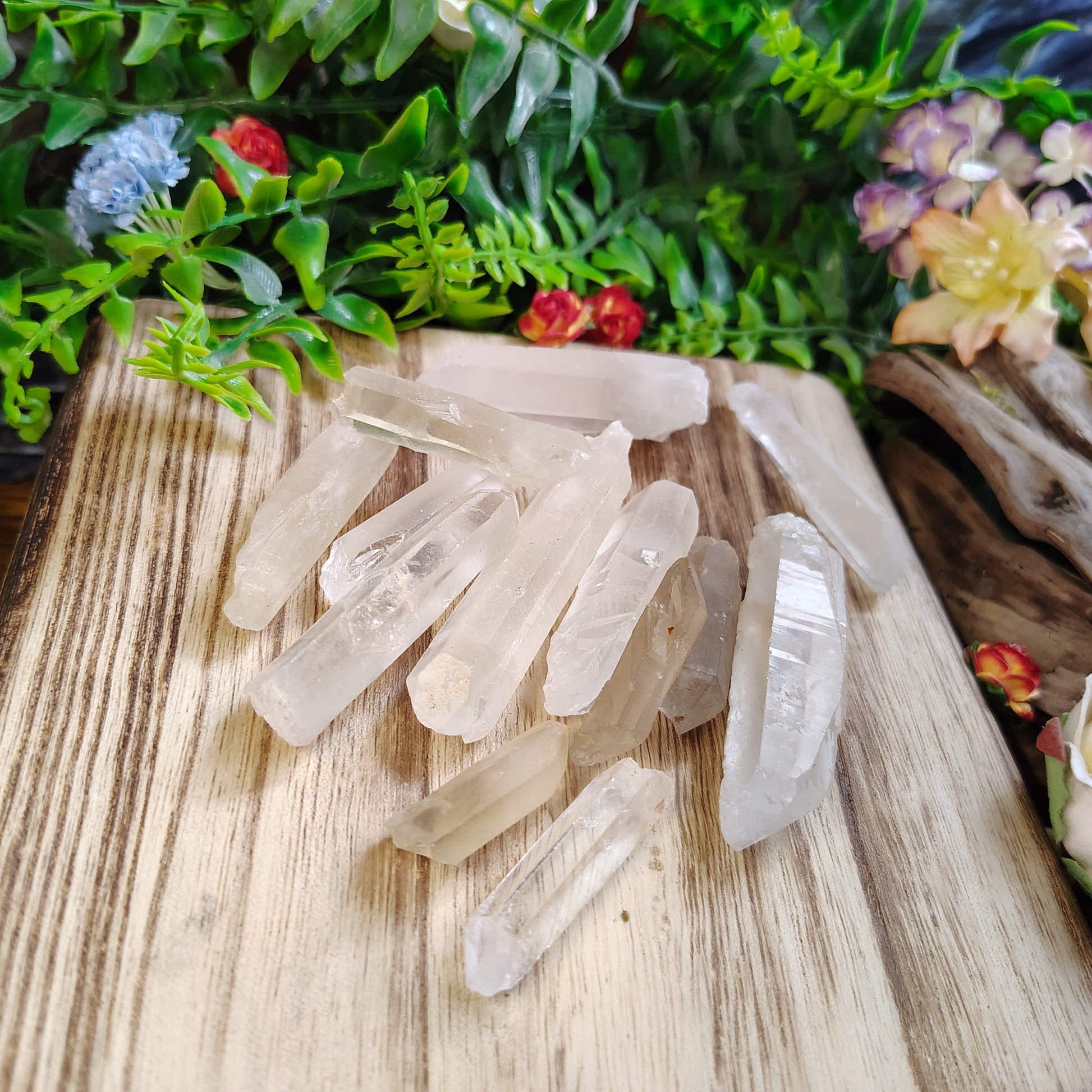 Clear crystal points on a wooden surface with greenery and flowers in the background