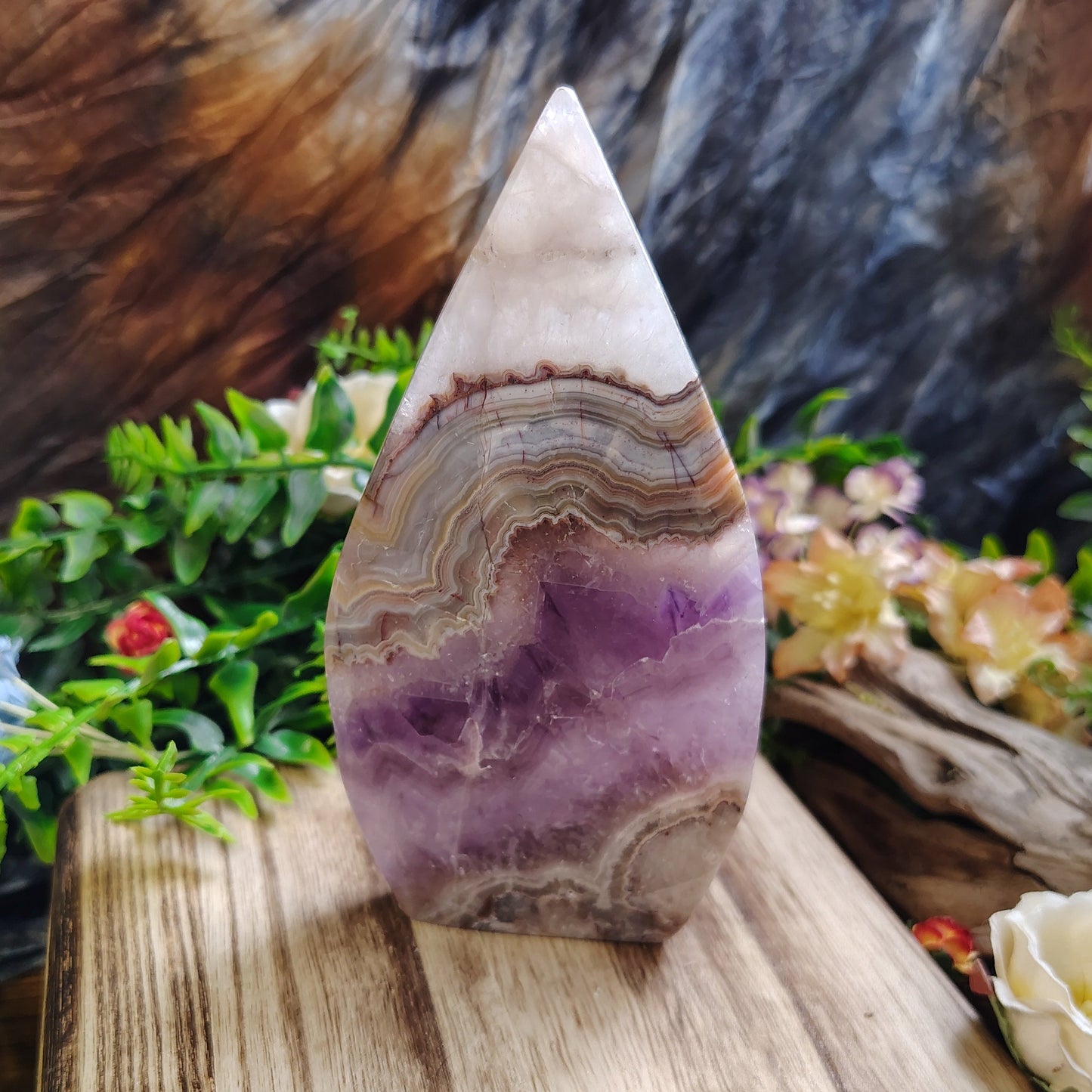 Polished agate stone on a wooden surface with plants and flowers in the background