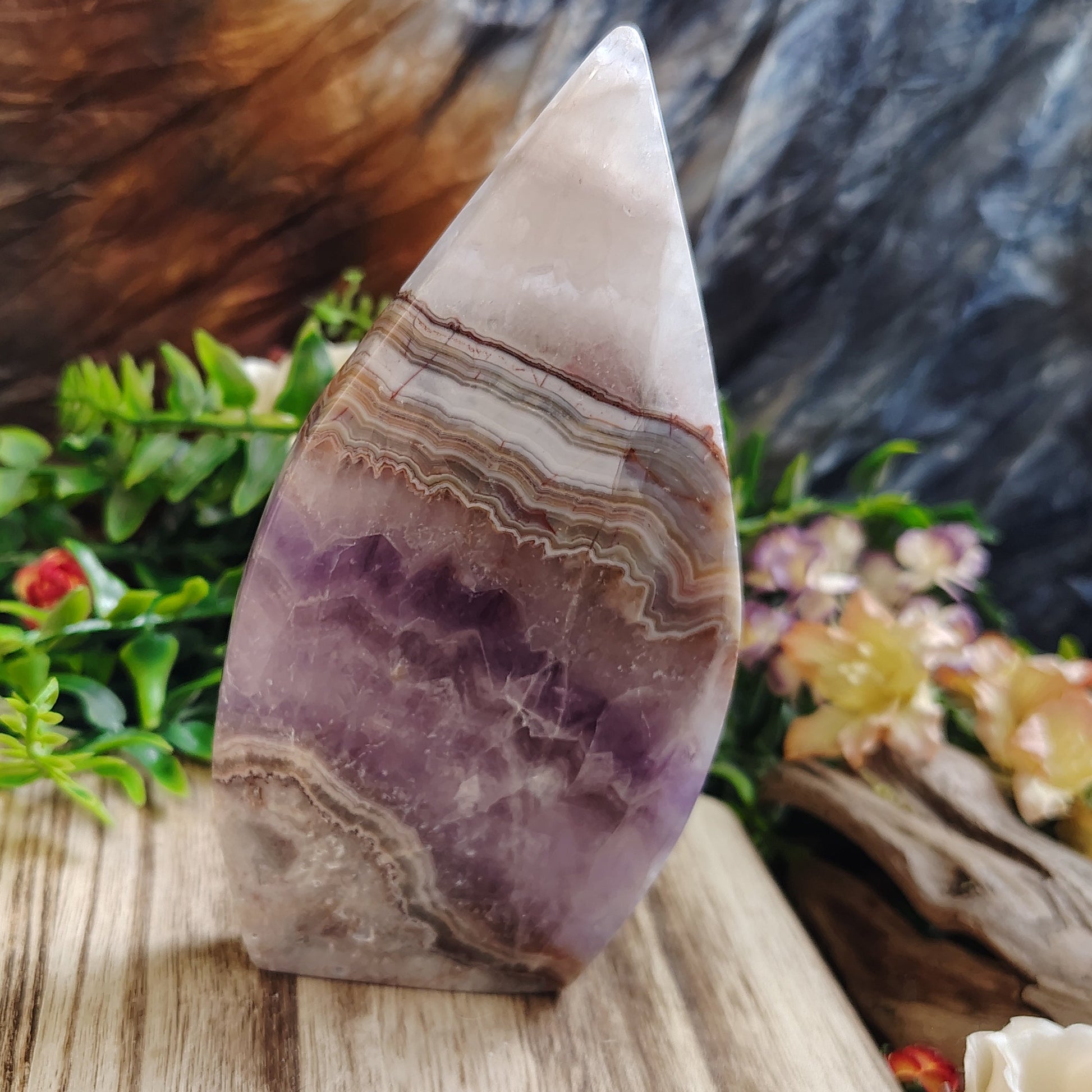 Agate and amethyst on a wooden surface with greenery and flowers in the background