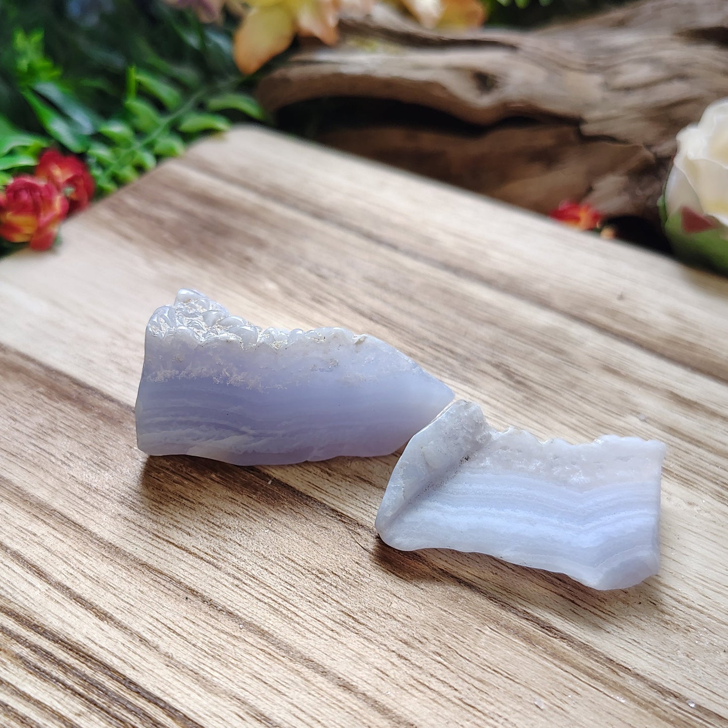 Two white crystals on a wooden surface with greenery and flowers in the background