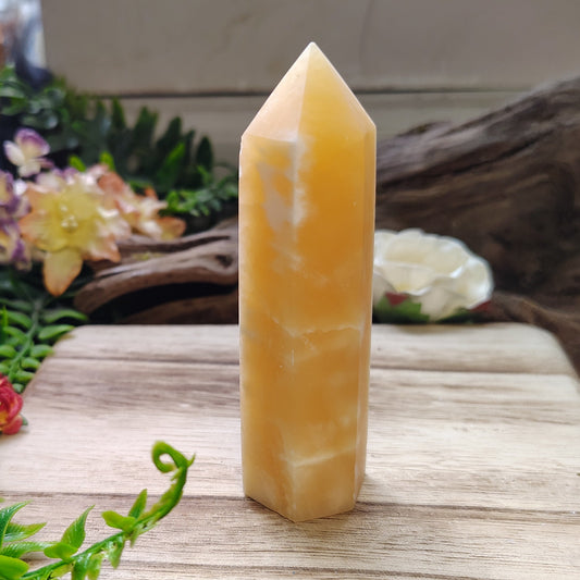 Tall, yellow crystal on a wooden surface with plants and flowers in the background