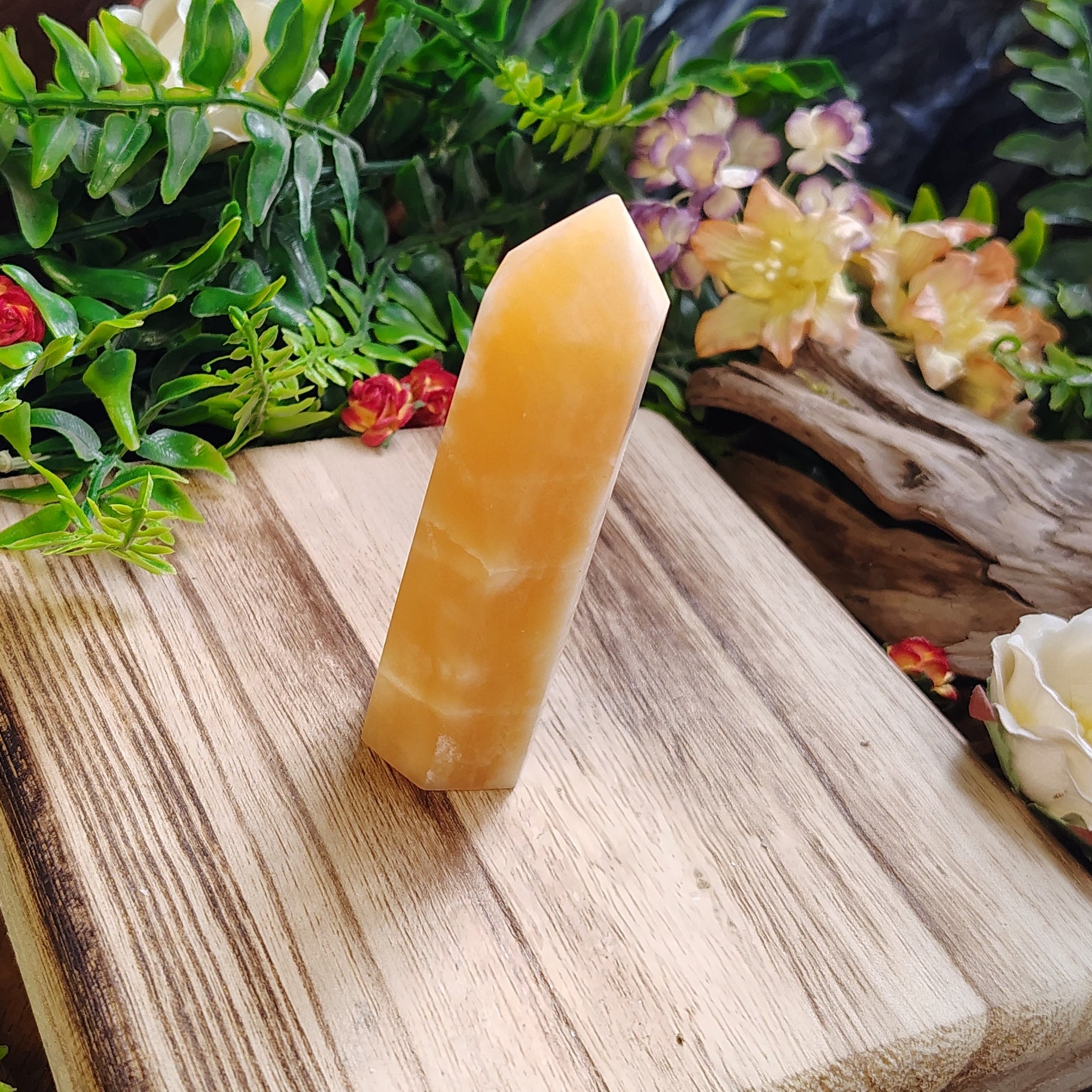 yellow crystal on a wooden block with greenery and flowers in the background