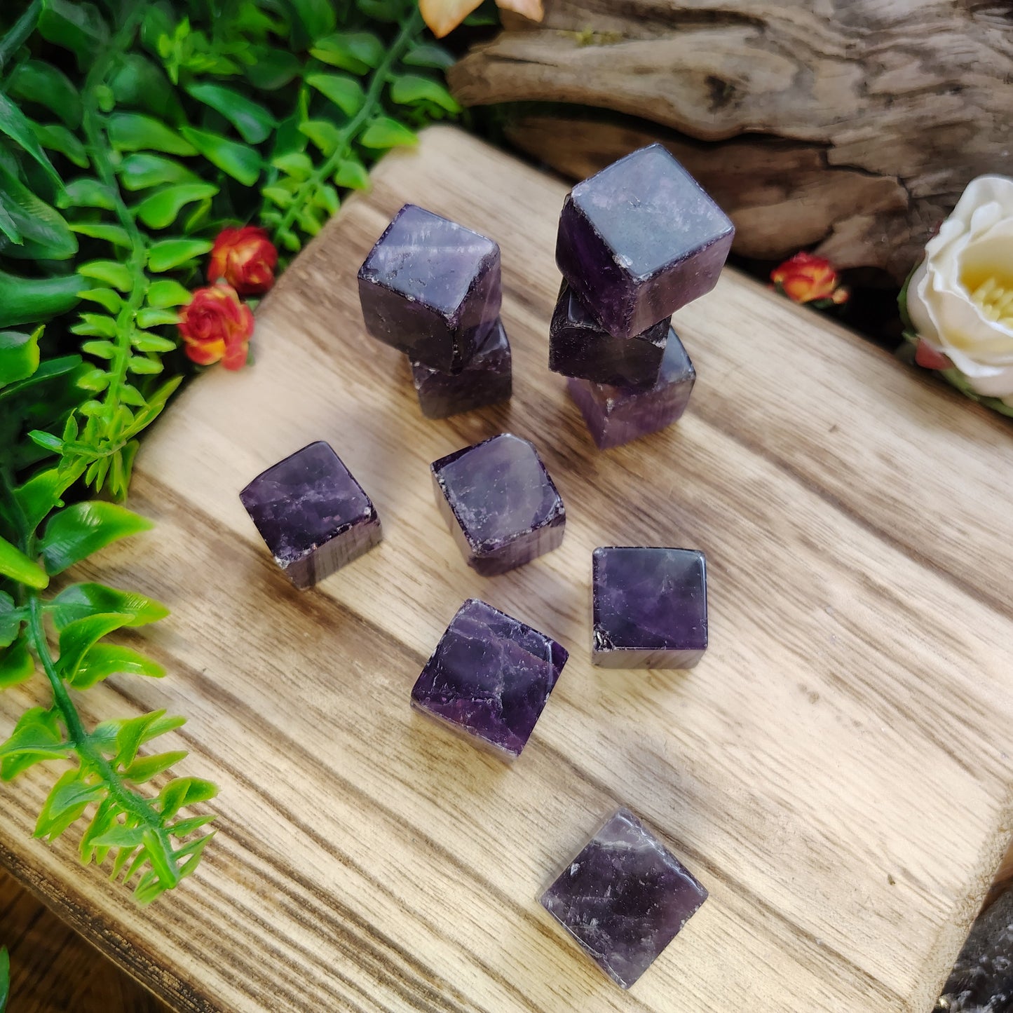 Purple crystal cubes on a wooden surface with greenery and flowers in the background