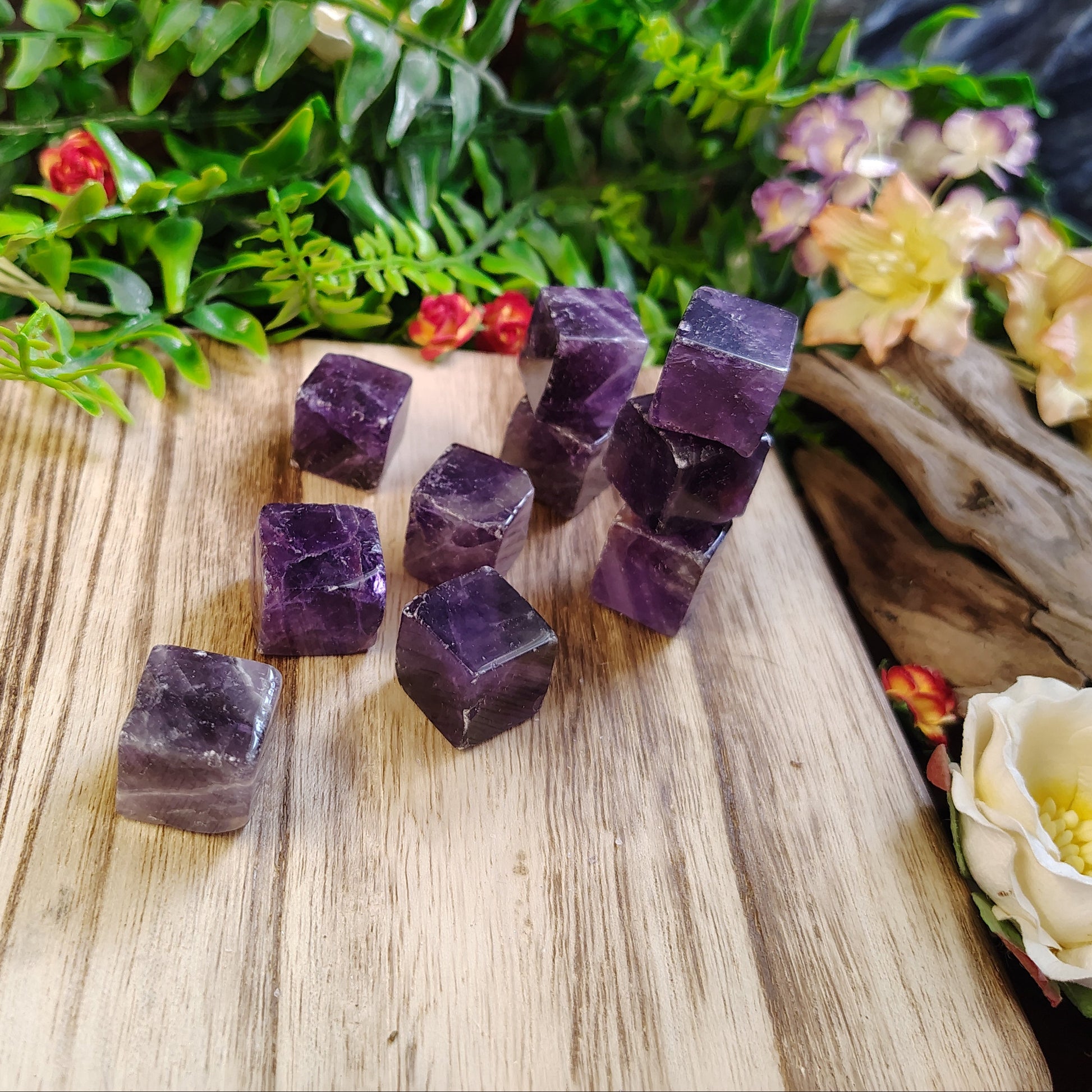 Purple crystal cubes on a wooden surface with greenery and flowers