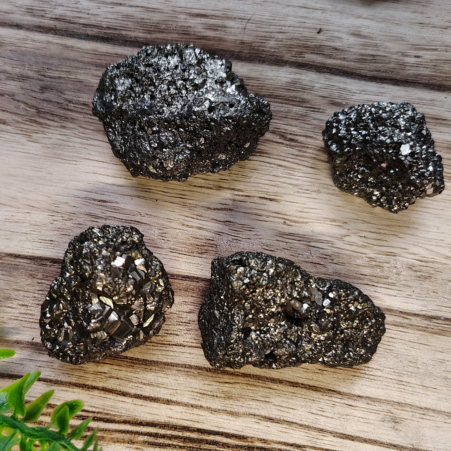 Four metallic rocks on a wooden surface with greenery around
