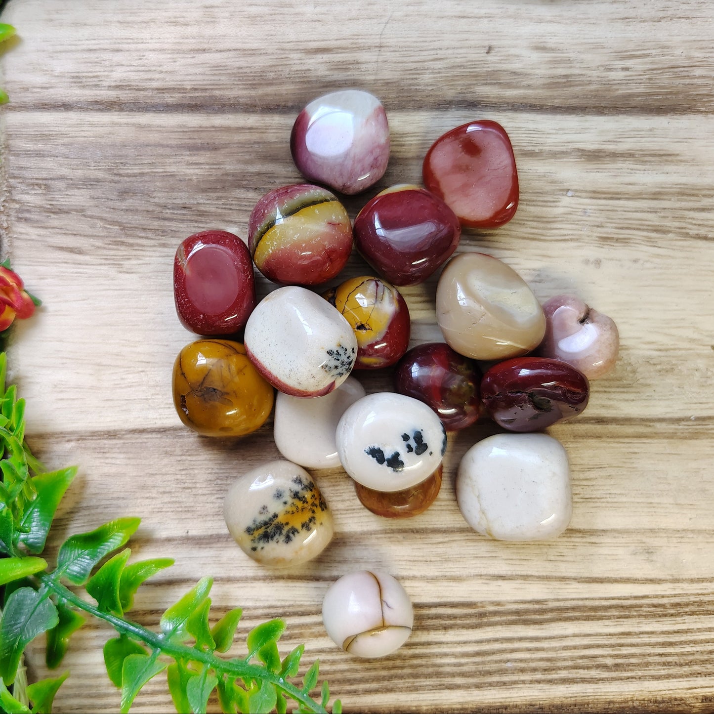 Multicolored gemstones on a wooden cutting board with green leaves on the side