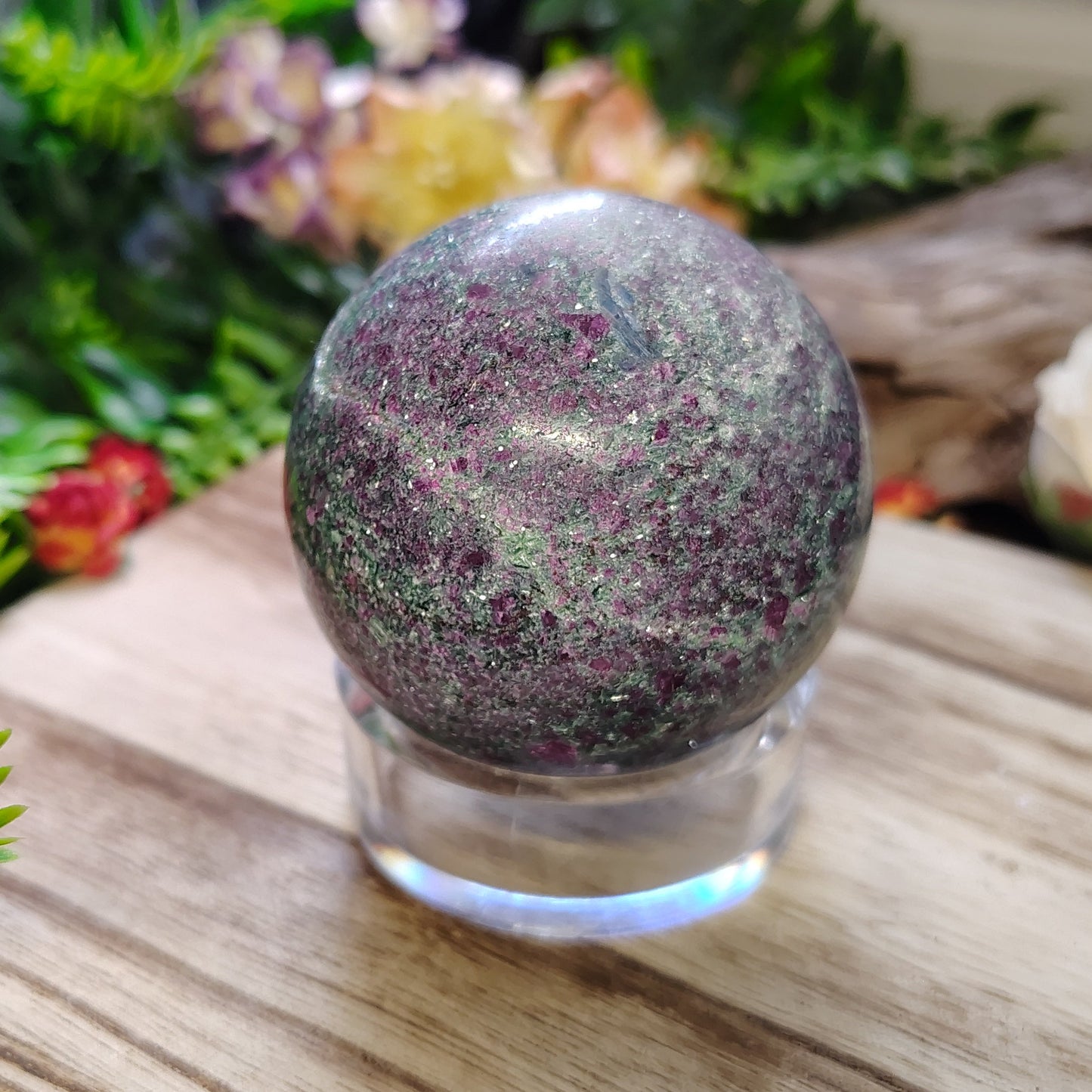 Decorative crystal ball on a wooden surface with greenery and flowers in the background