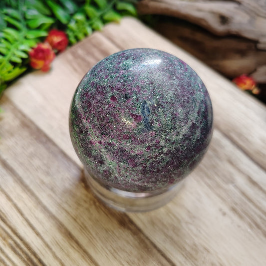 Multicolored crystal ball on a wooden surface with greenery and flowers in the background