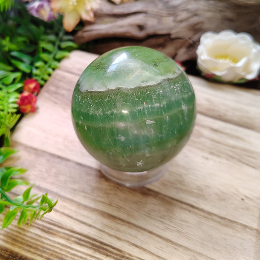 Green crystal ball on a wooden surface with plants and flowers in the background