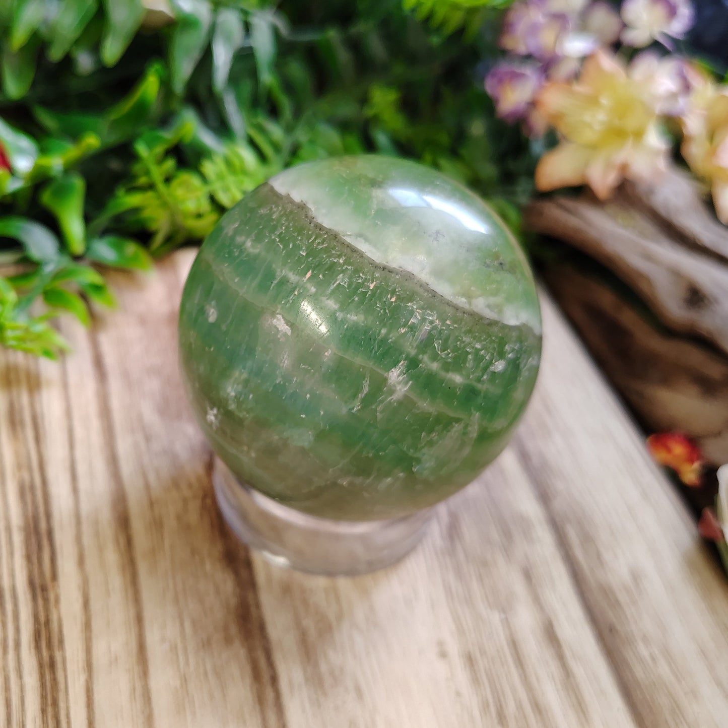 Green crystal ball on a wooden surface with plants and flowers in the background