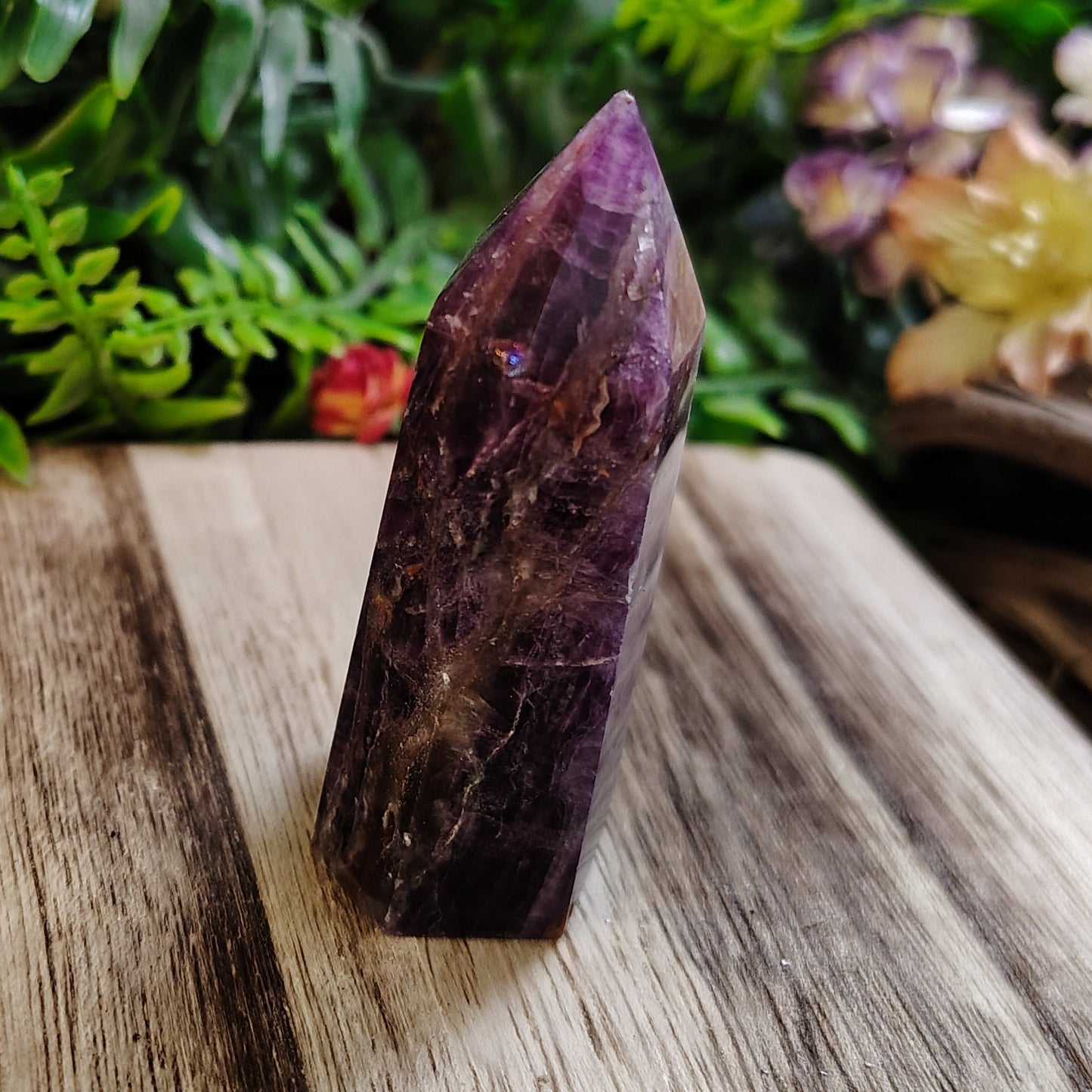 Amethyst crystal on a wooden surface with greenery and flowers in the background