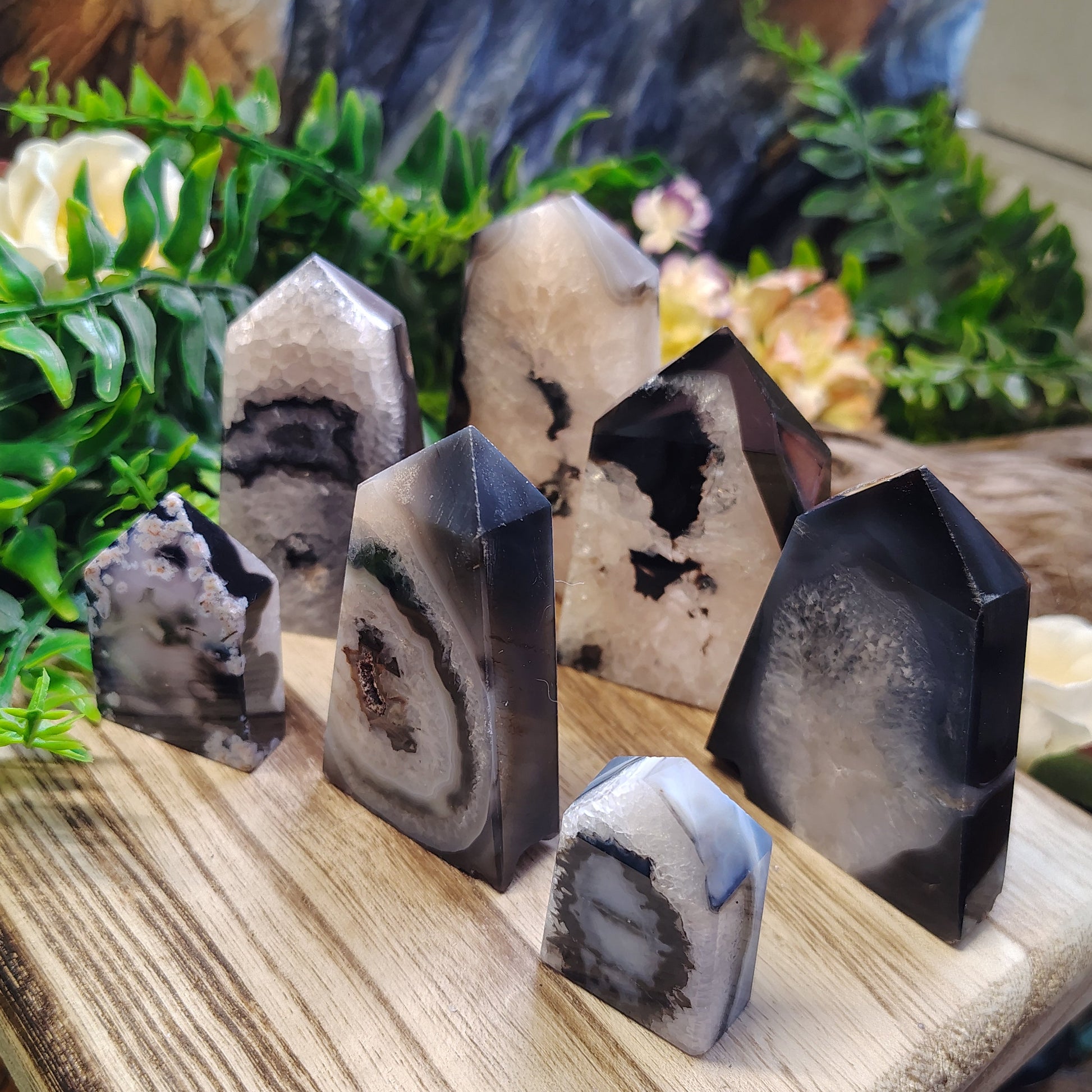 Collection of agate stones on a wooden stand with greenery and driftwood in the background