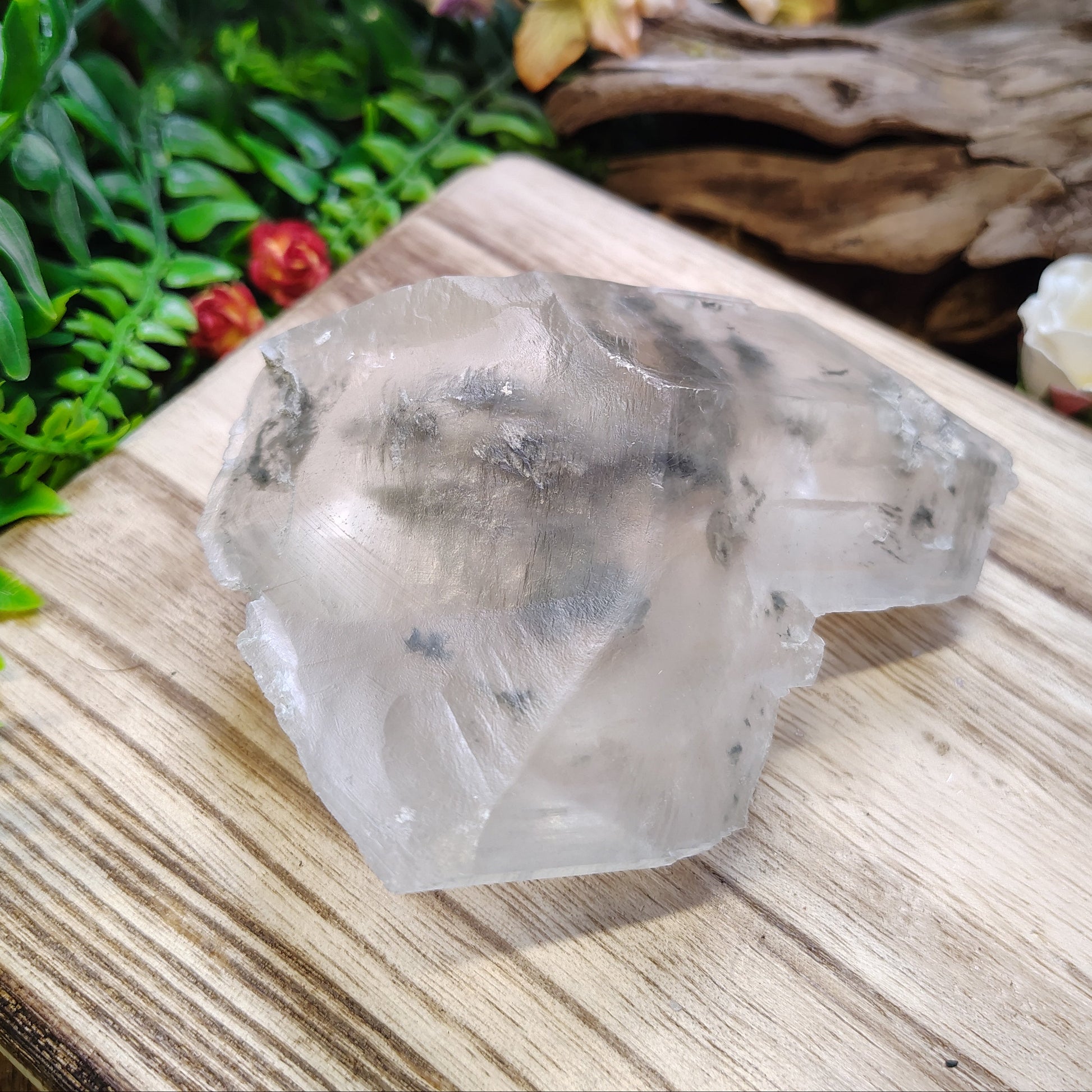 Clear crystal on a wooden surface with plants and flowers in the background