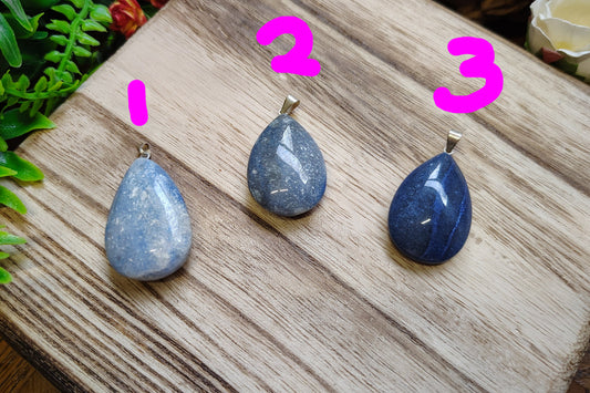 Three blue teardrop-shaped pendants on a wooden surface with greenery in the background