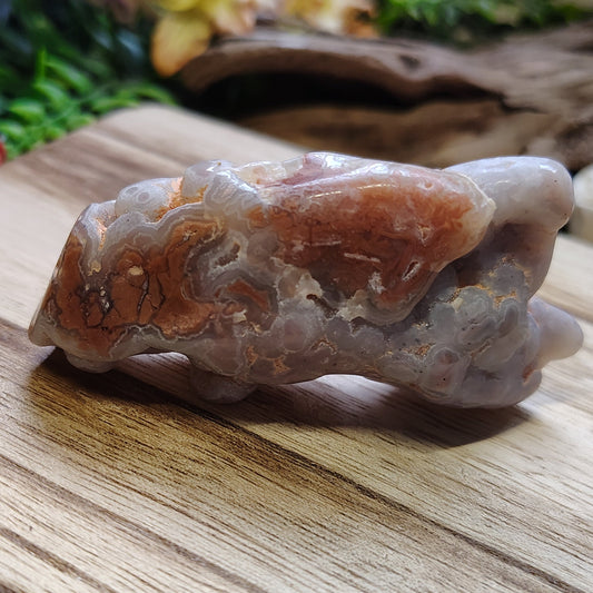 Raw crystal on a wooden surface with greenery in the background