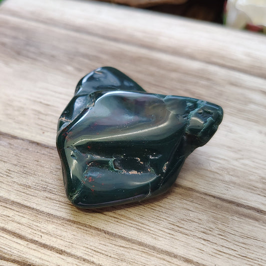 Polished bloodstone on a wooden surface with greenery in the background