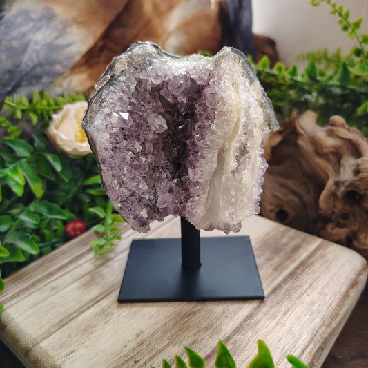 Amethyst crystal on a stand with natural wood and greenery in the background