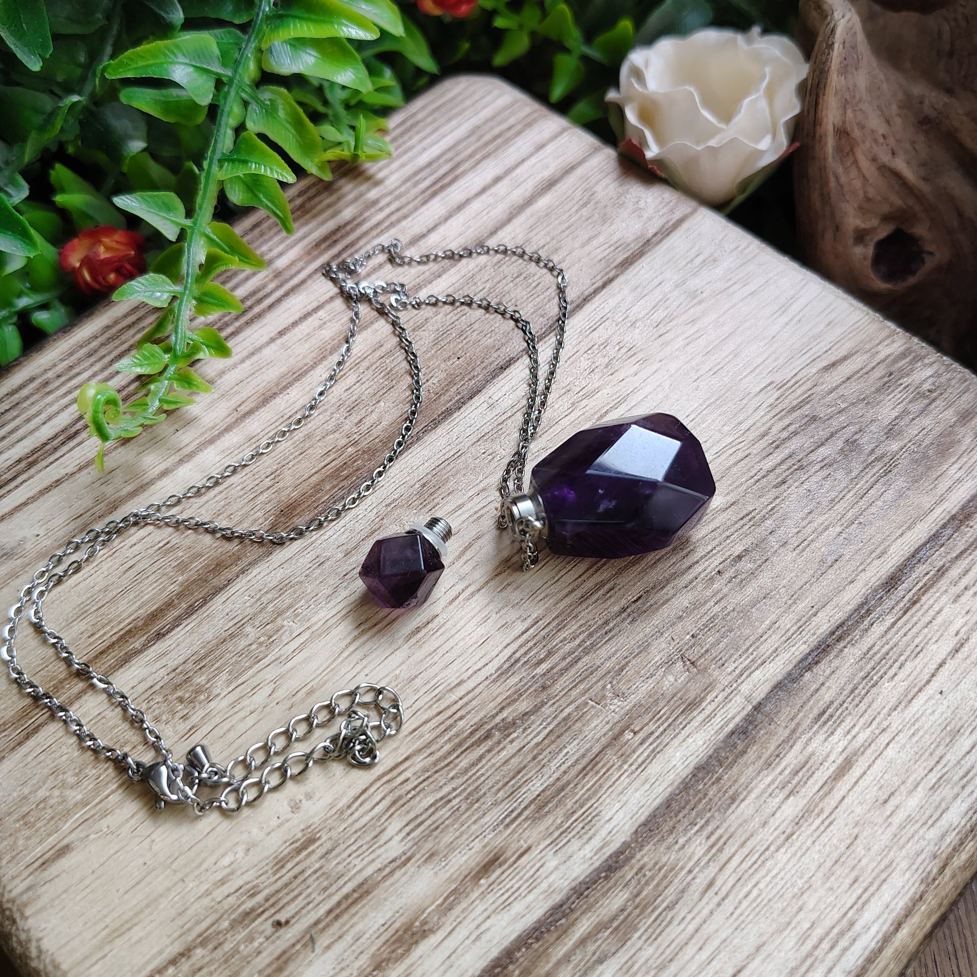 Necklace with an amethyst pendant on a wooden surface surrounded by flowers and greenery