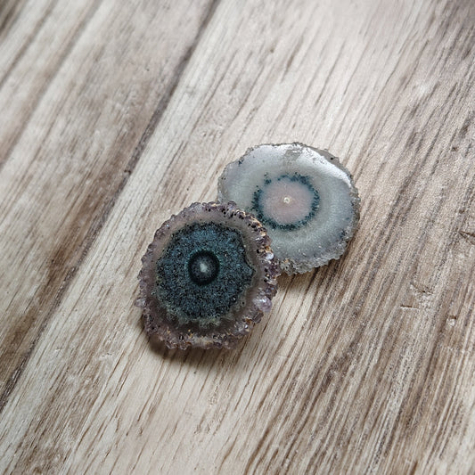 Two small round stones on a wooden surface with greenery in the background