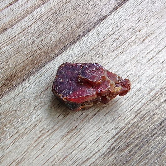 Small red stone on a wooden surface with greenery in the background