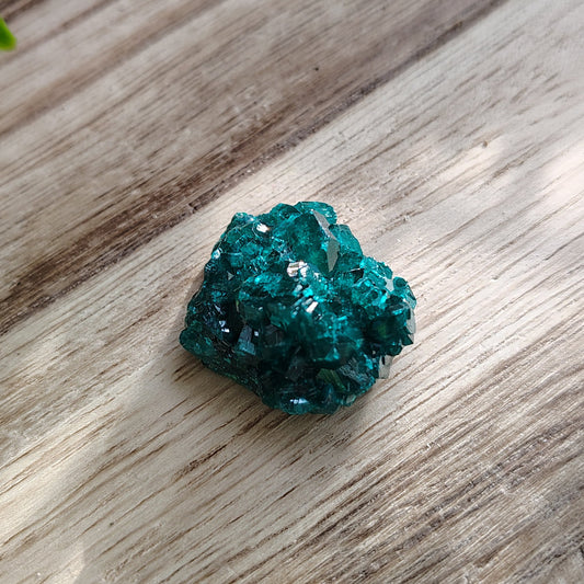 Green crystal on a wooden surface with plants in the background