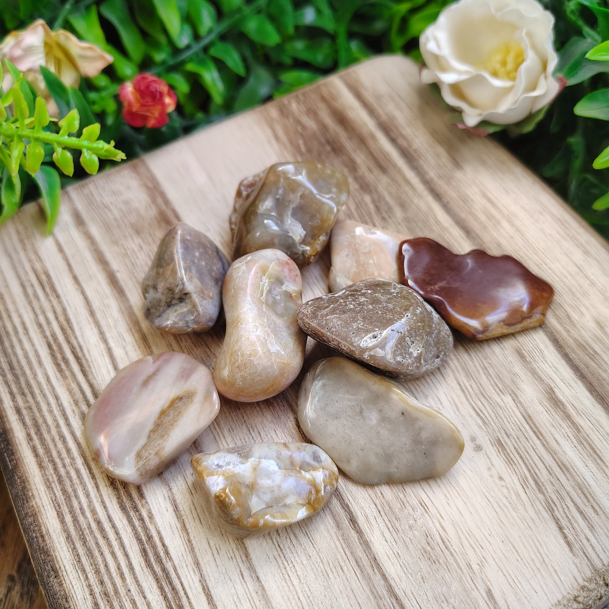 Collection of polished stones on a wooden surface with flowers in the background