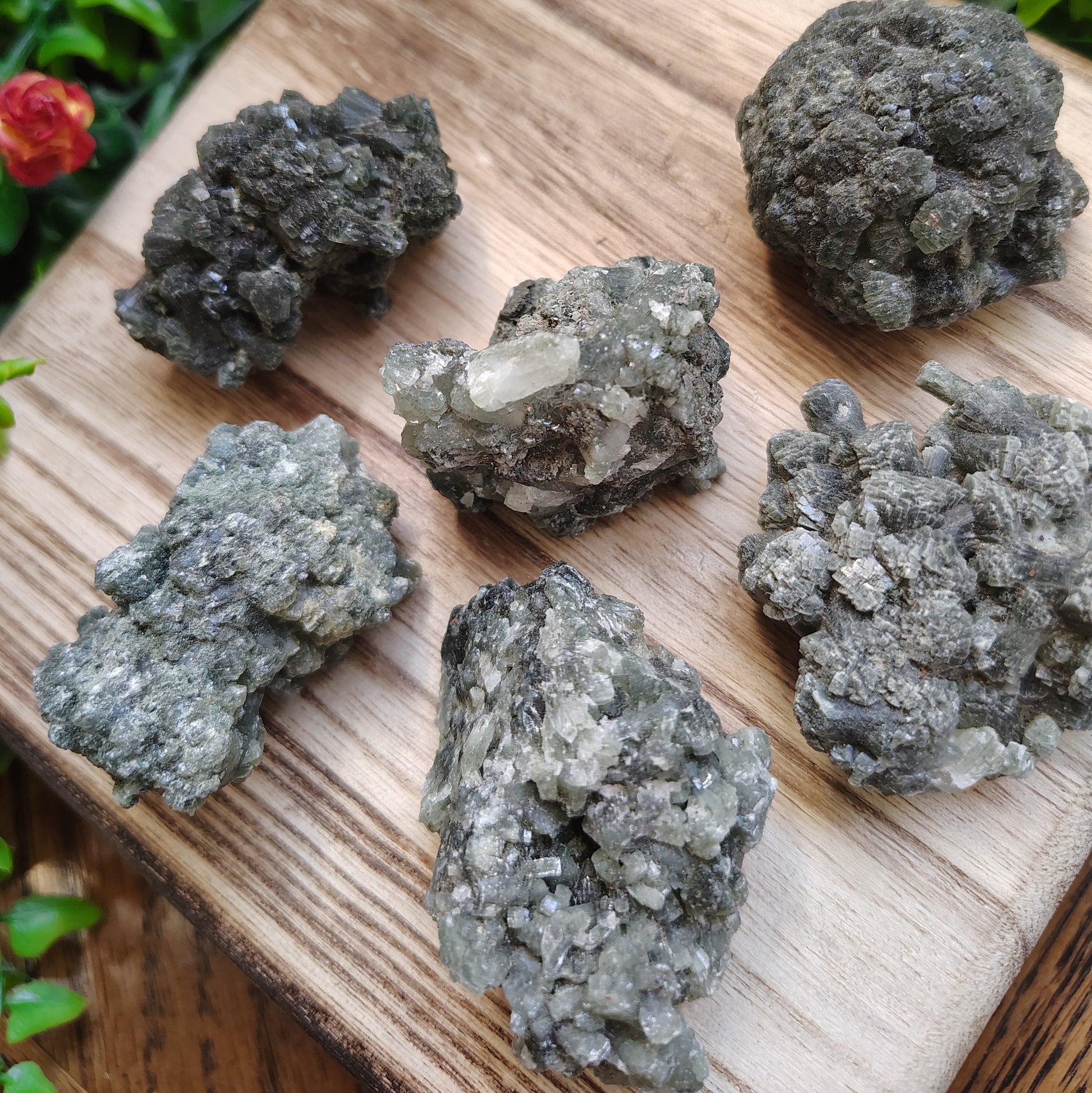 Mineral specimens on a wooden board with greenery and flowers in the background