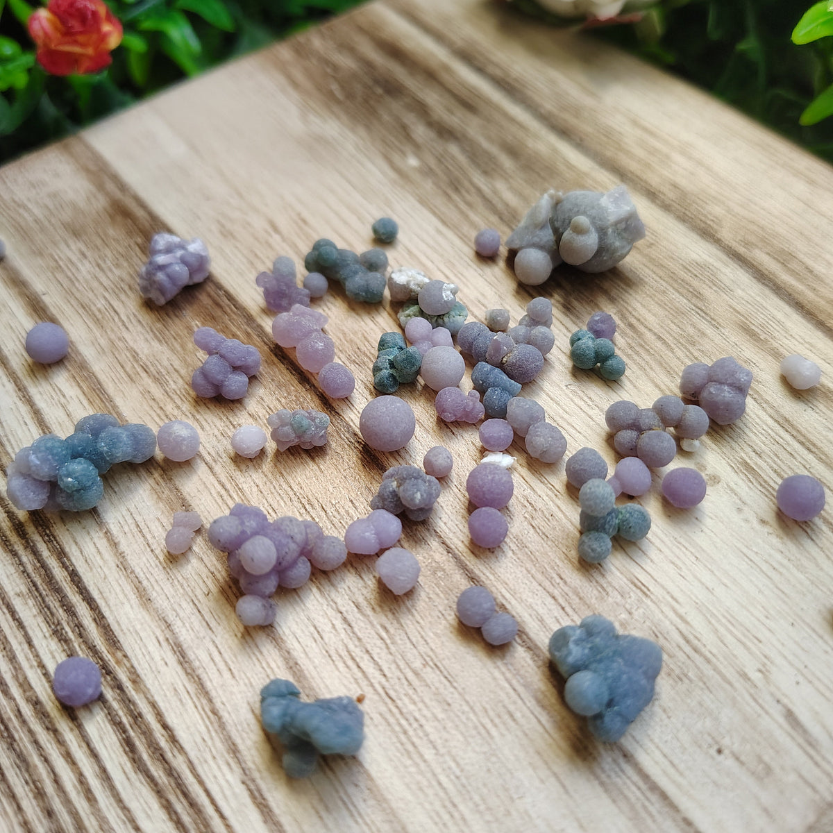Small purple and gray stones on a wooden surface with greenery in the background