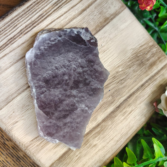 Raw fluorite on a wooden surface with greenery and flowers in the background