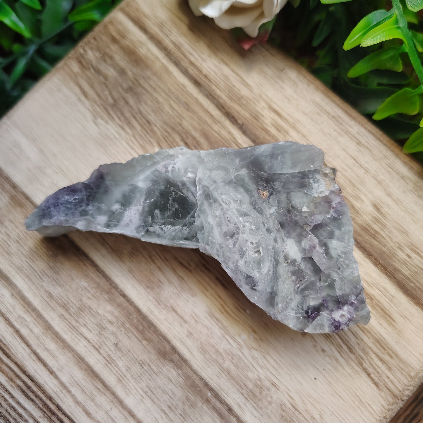 Crystal on a wooden surface with greenery and a flower in the background