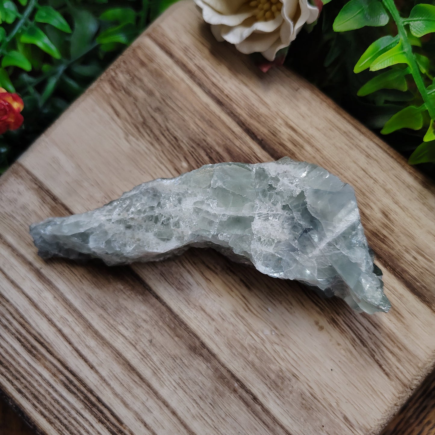 Crystal on a wooden surface with greenery and a flower in the background