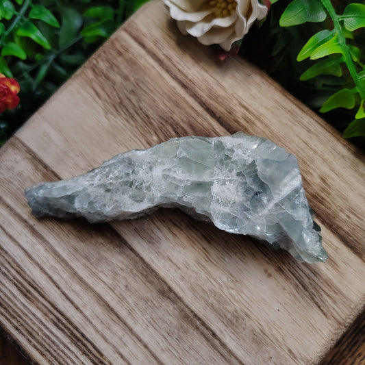 Crystal on a wooden surface with greenery and a flower in the background