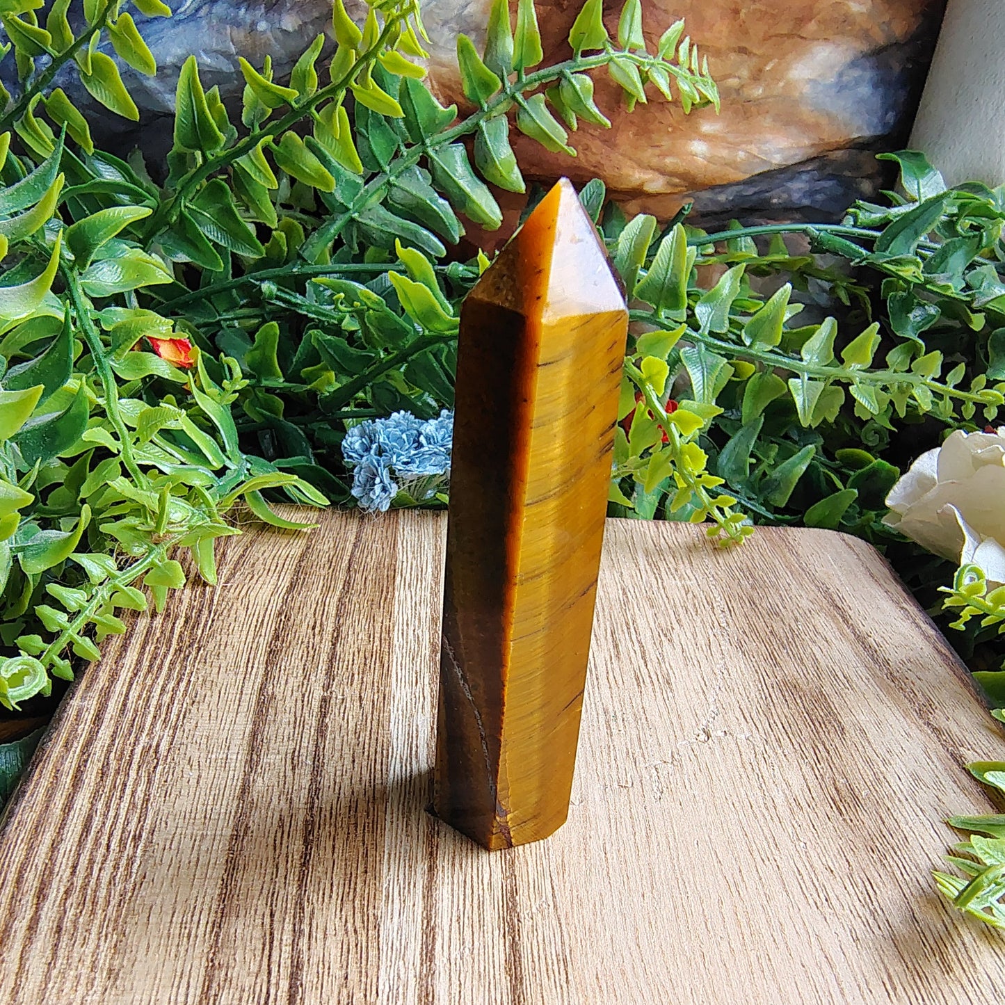 Tiger's eye crystal on a wooden surface with greenery and flowers