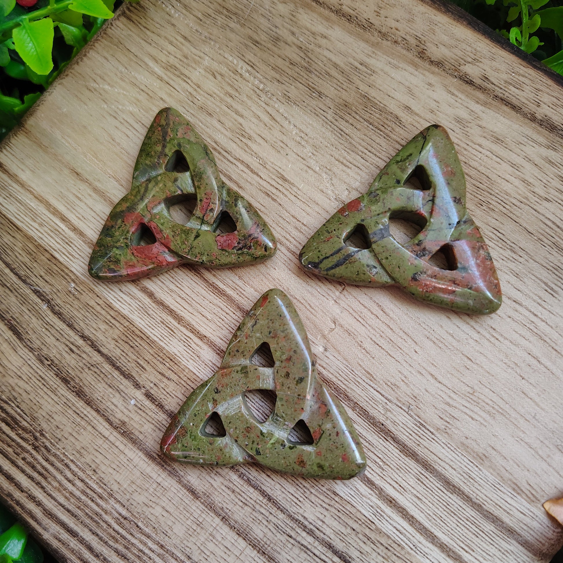 Three green stone triangular pieces with cut-out patterns on a wooden surface.