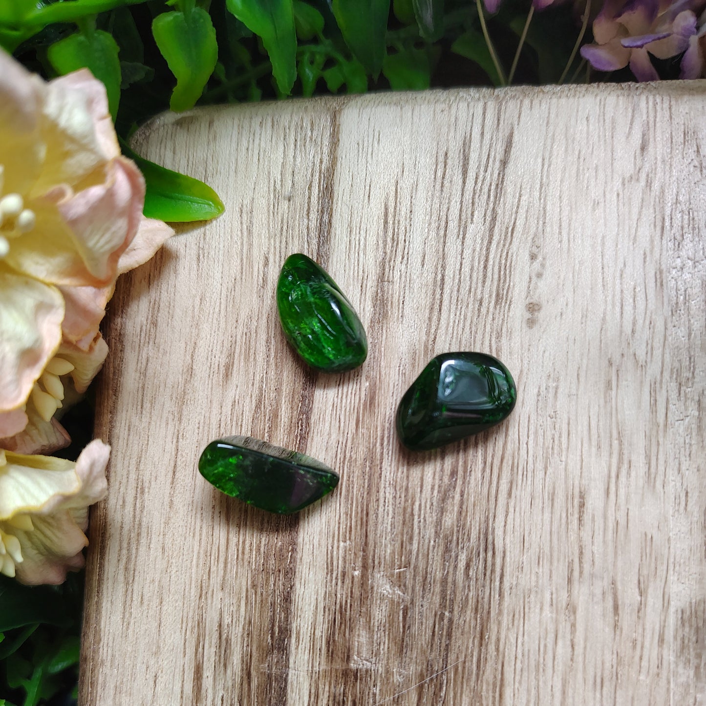 Three green gemstones on a wooden surface with flowers around