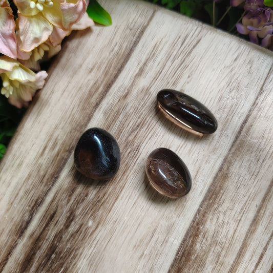 Three dark stones on a wooden surface with flowers in the background