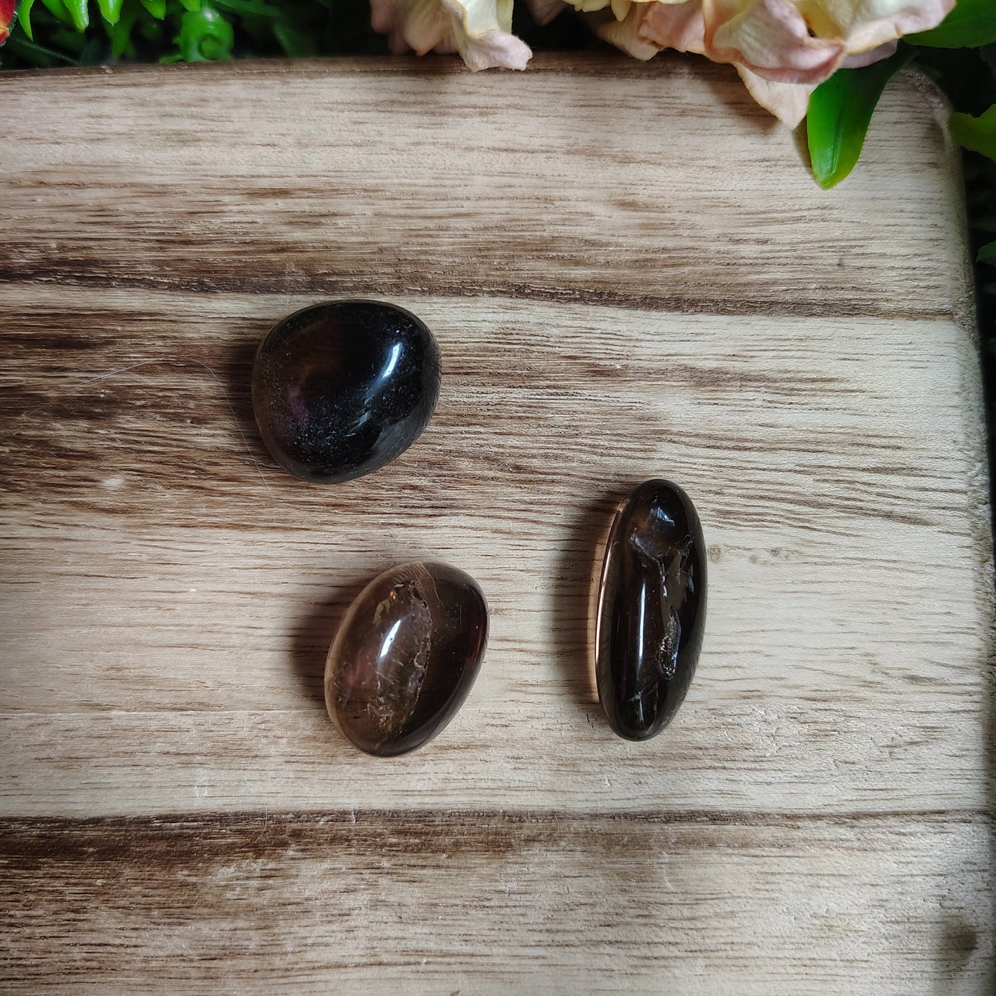 Three dark stones on a wooden surface with flowers in the corner